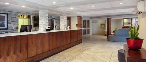 A modern reception area with a wooden counter, stone pillars, and a herringbone-patterned floor.