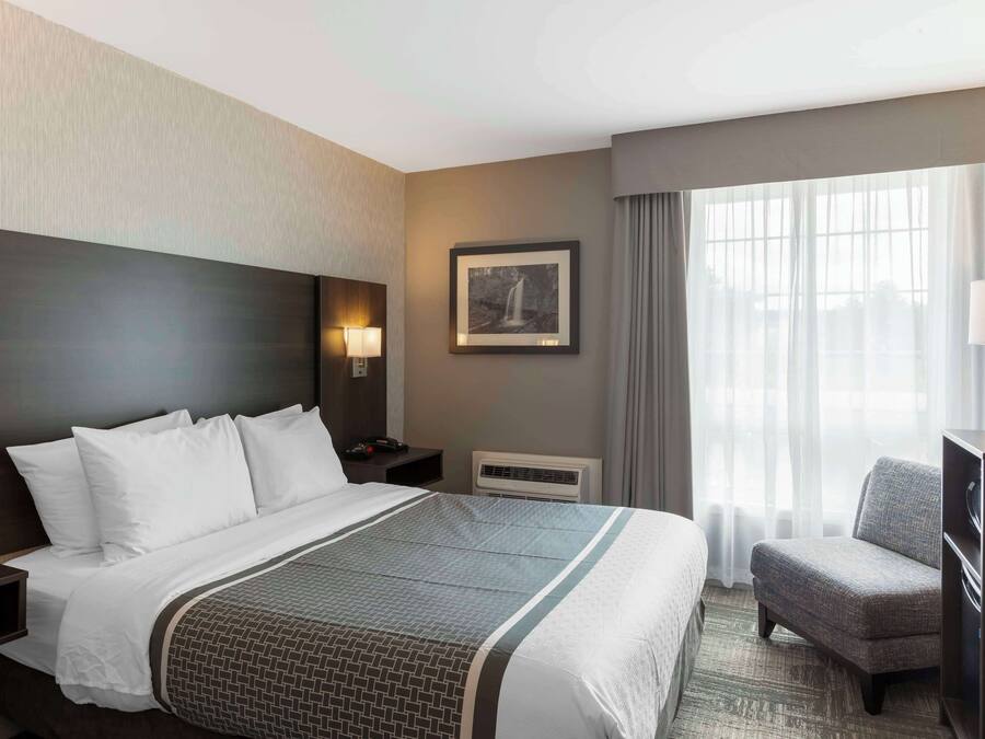 A hotel room with a large bed, a chair, a desk, a picture on the wall, and a window with curtains.