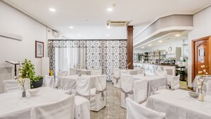 Una sala conferenze con tavoli apparecchiati per una riunione, un’area bar sullo sfondo e una pianta decorativa in primo piano.