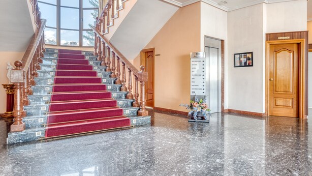 Un'imponente scalinata con gradini in marmo e tappeto rosso, che conduce a un soffitto alto con un lampadario.