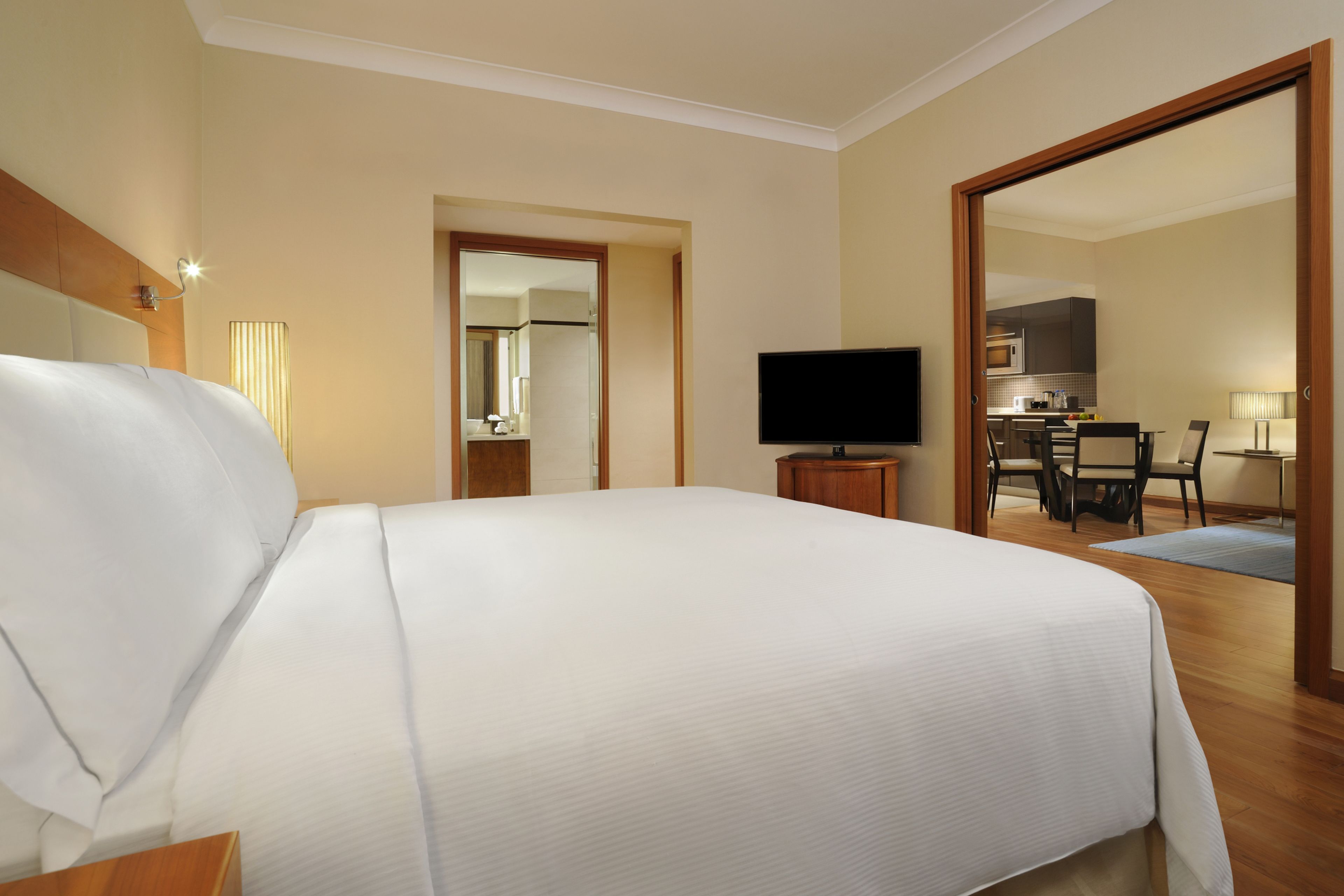 A hotel room with a large bed, a television, a desk with a chair, and a view into the kitchen area.