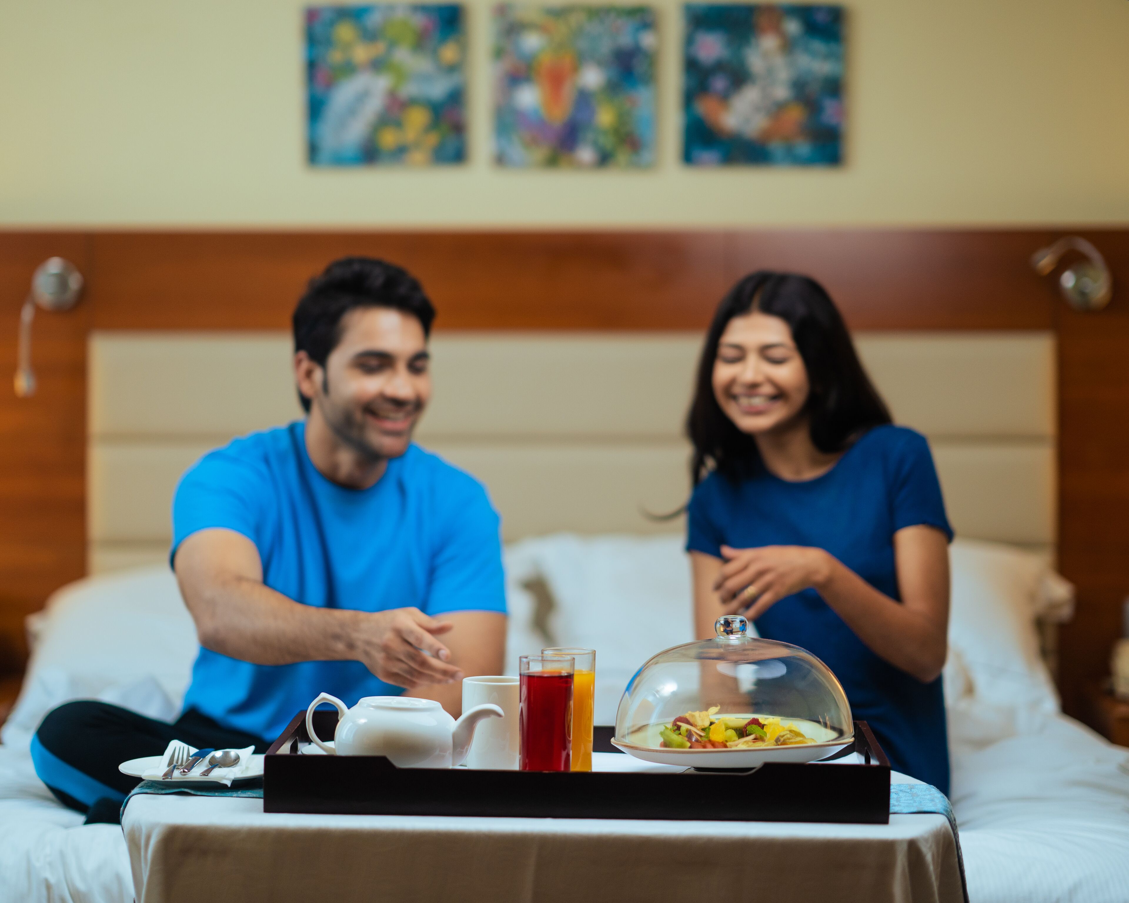 Una habitación de hotel con una cama, una bandeja de desayuno y obras de arte en la pared.