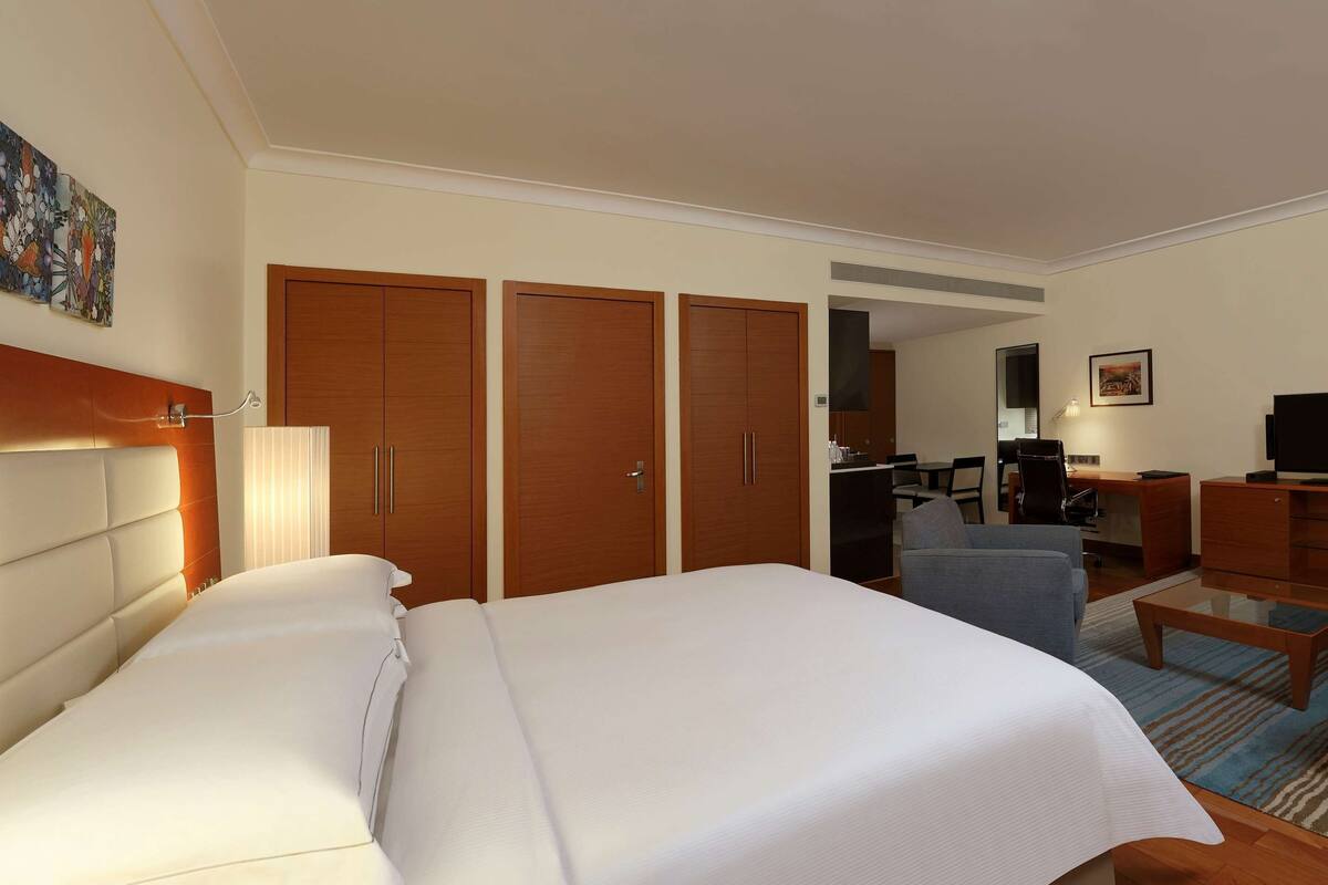 A hotel room with a large bed, a desk, a chair, a sofa, and a television.