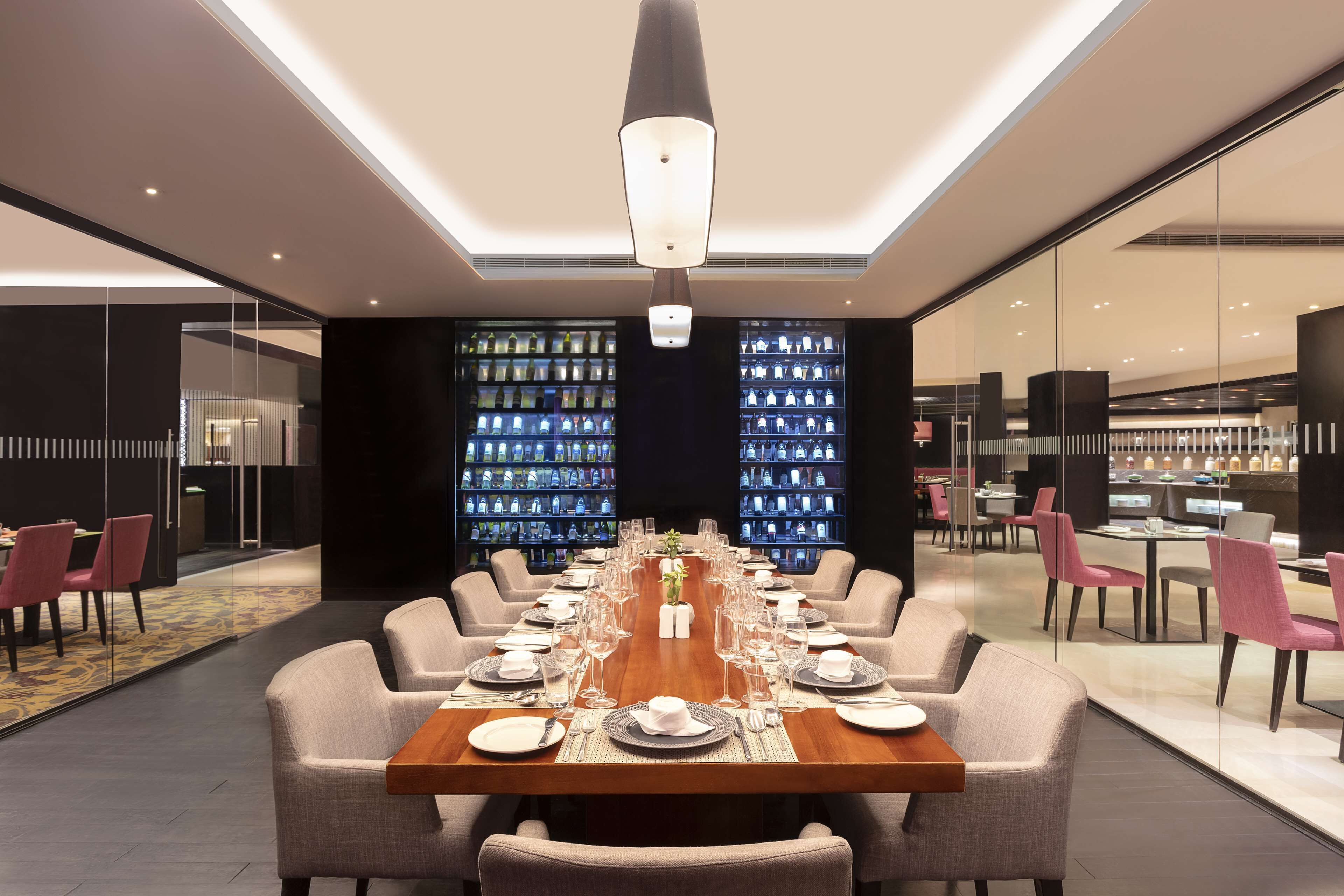 A modern dining area with a long table set for a meal, surrounded by chairs, and a large chandelier above.