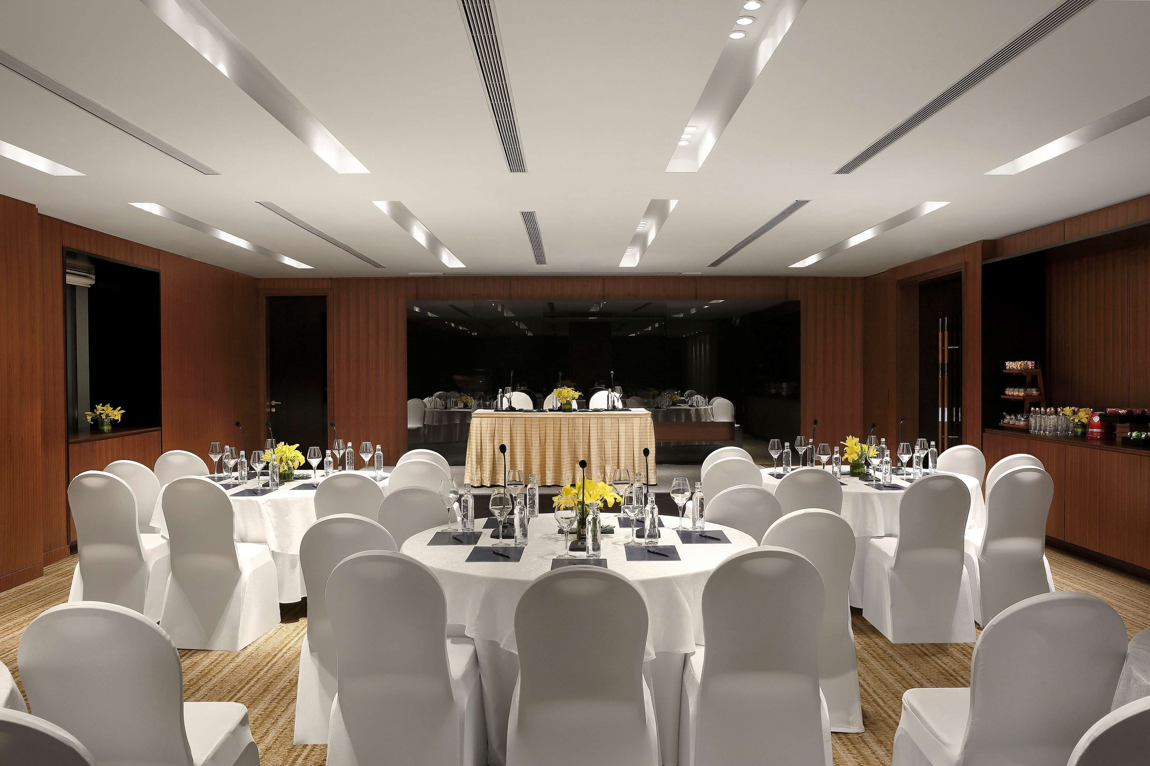 A conference room with round tables, white chairs, and a stage with a tablecloth.