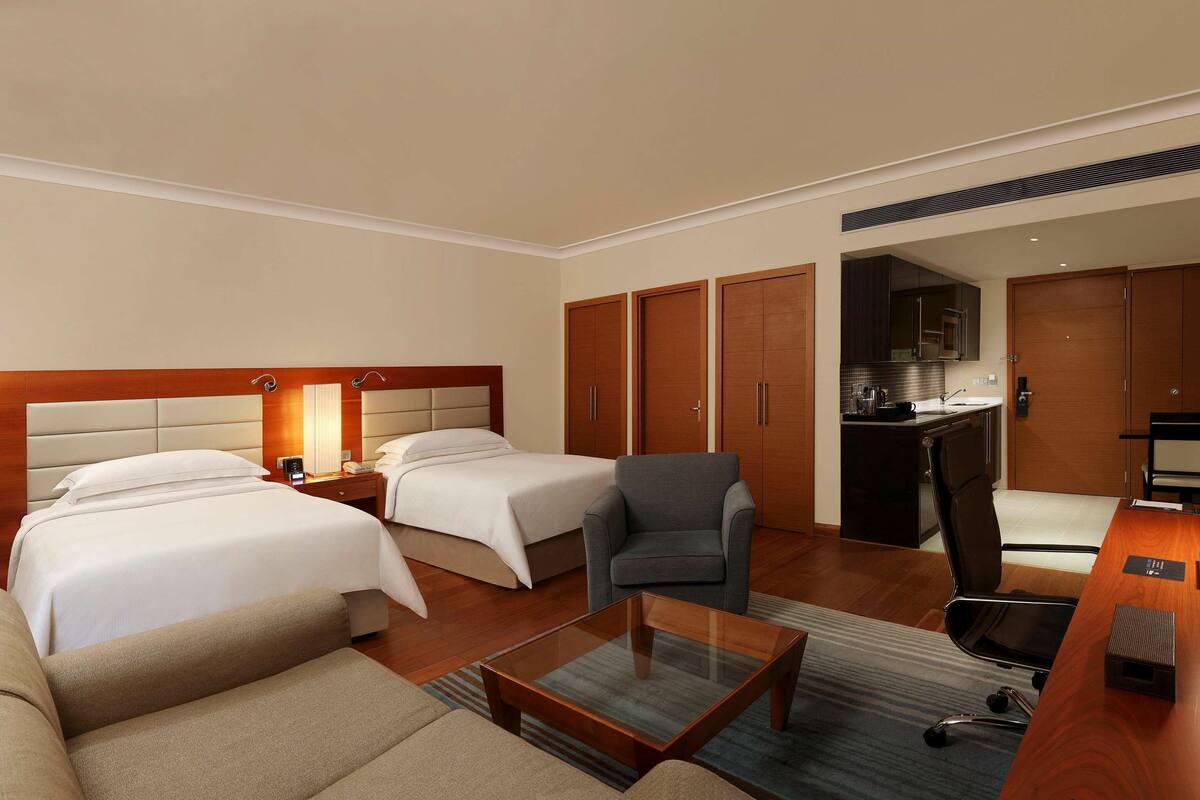 A hotel room with two beds, a sofa, a desk with a computer, a chair, and a TV.