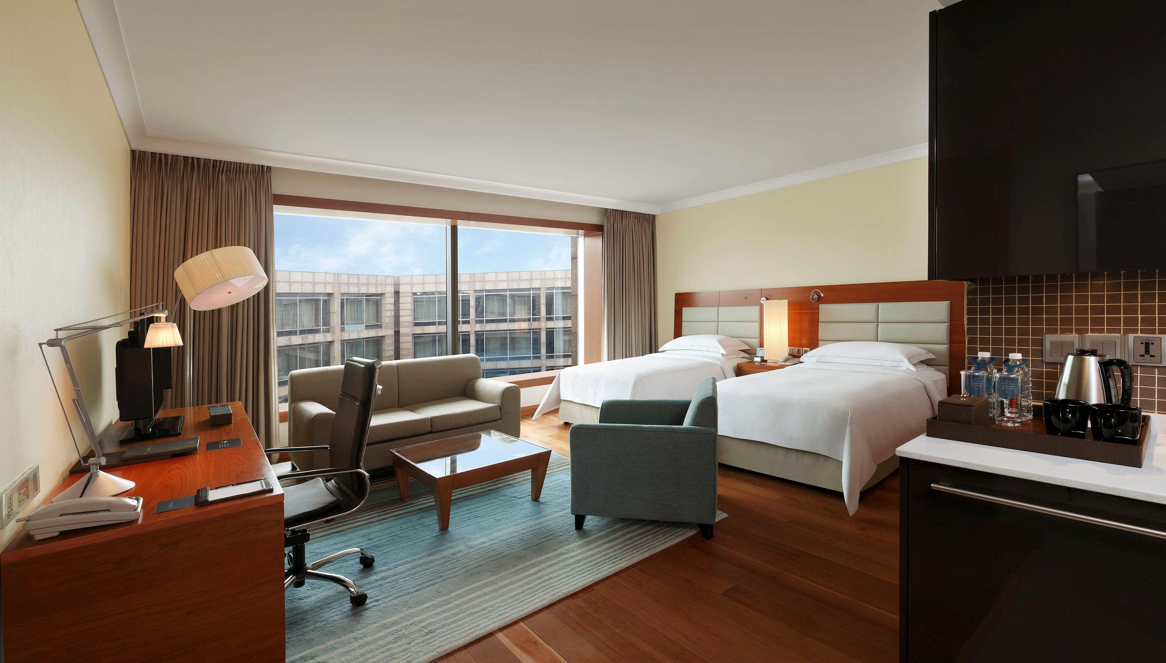 A hotel room with two beds, a desk, a chair, a coffee maker, and a view of the city.