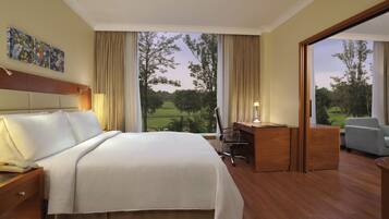 A hotel room with a large bed, a desk with a chair, a sofa, and a view of a golf course.