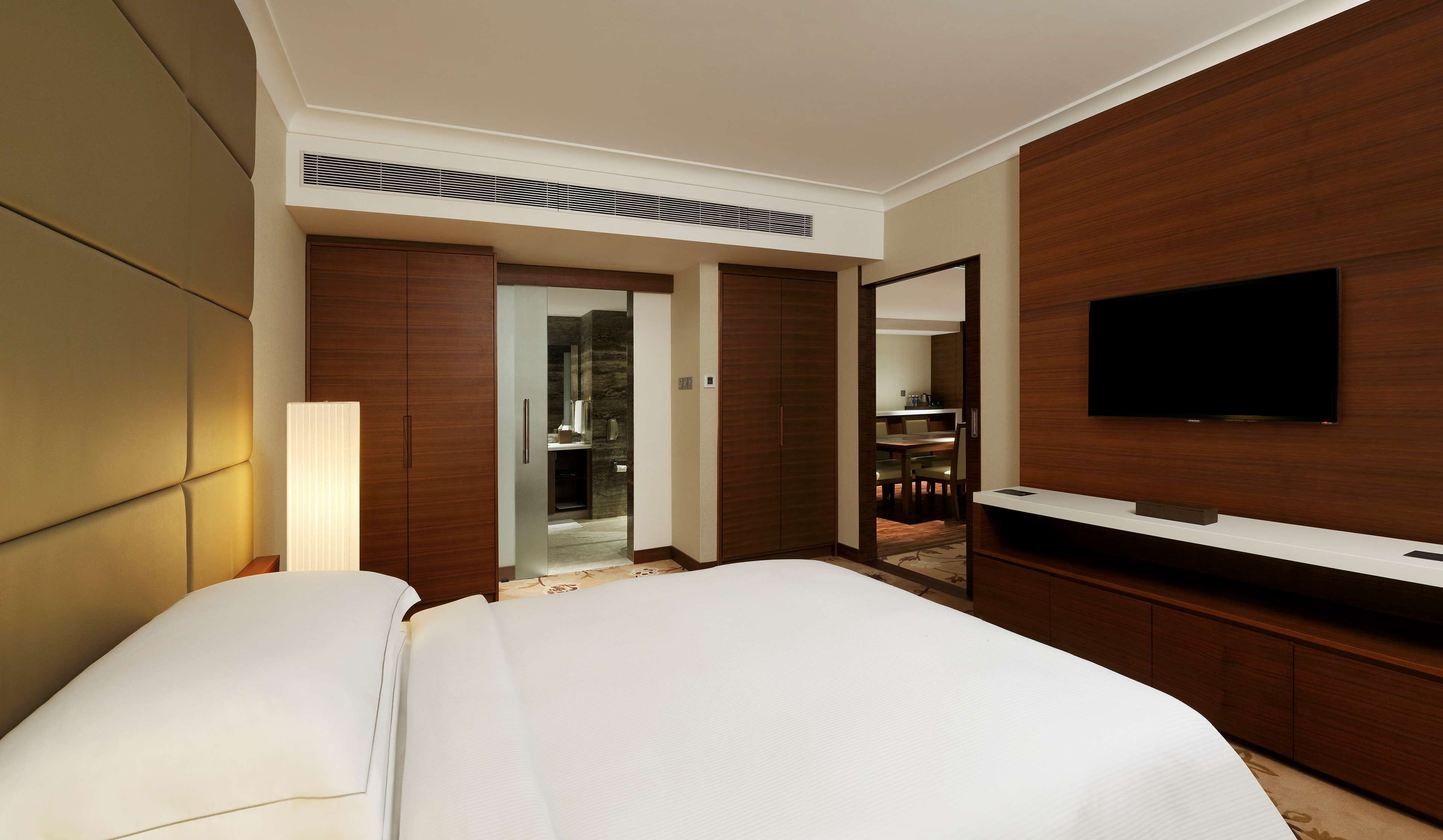 A hotel room with a large bed, a TV mounted on the wall, a wardrobe, and a bathroom visible through an open door.
