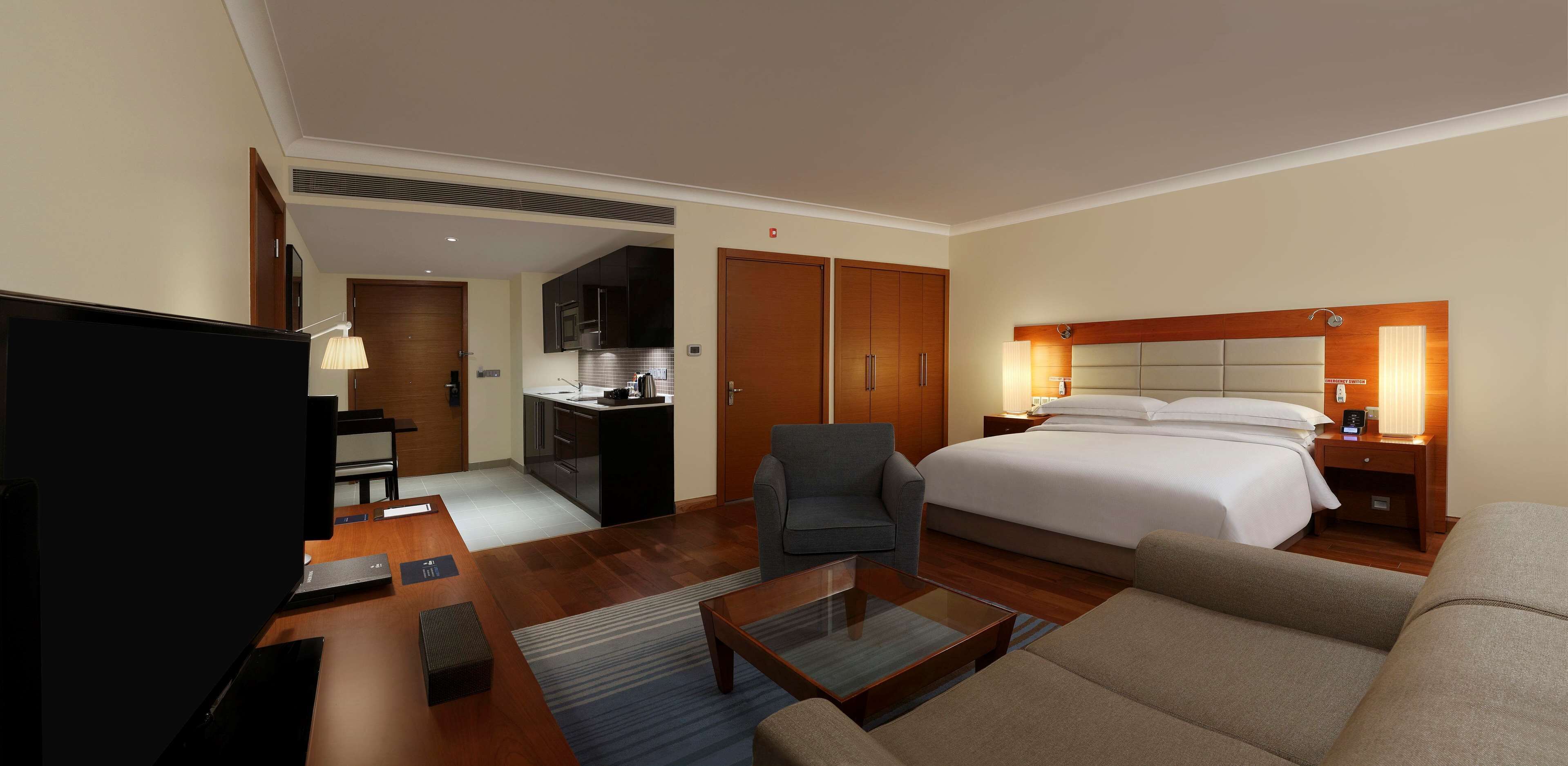 A hotel room with a bed, a TV, a desk, a chair, and a kitchenette.