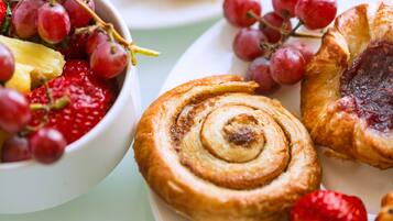 A plate with a cinnamon roll, strawberries, and red grapes.