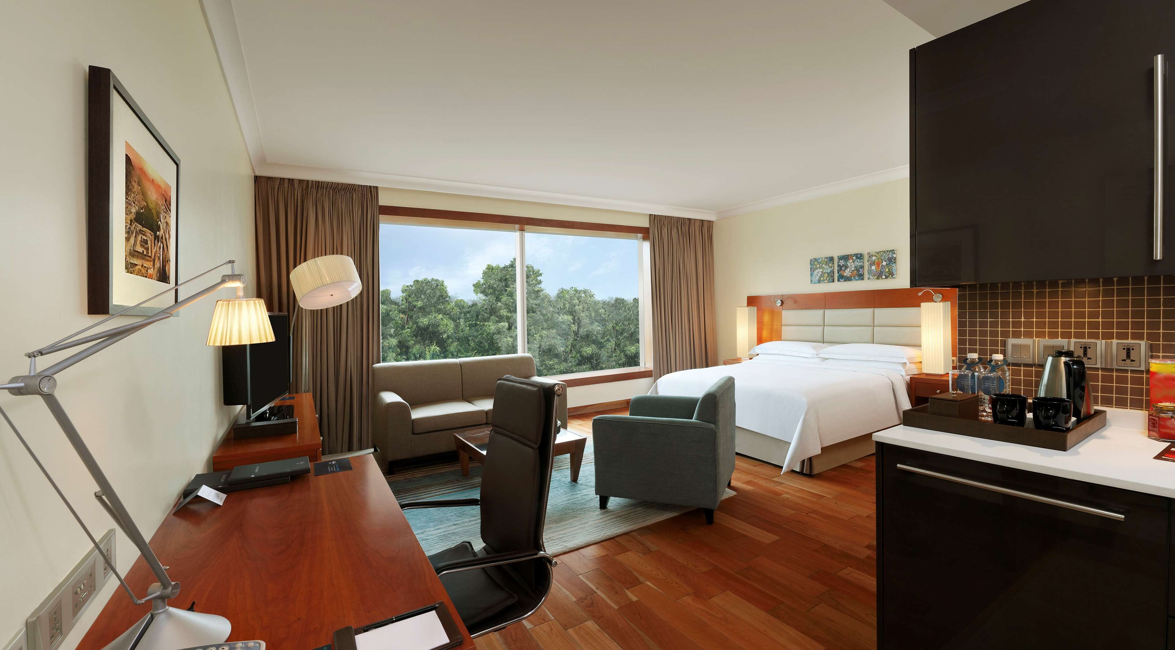 A hotel room with a bed, a desk with a lamp, a chair, and a view of the outdoors.