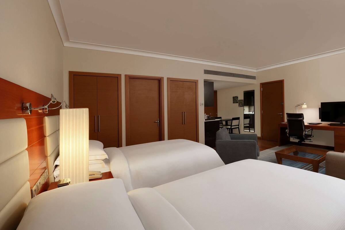 A hotel room with two beds, a desk, a TV, and a lamp.