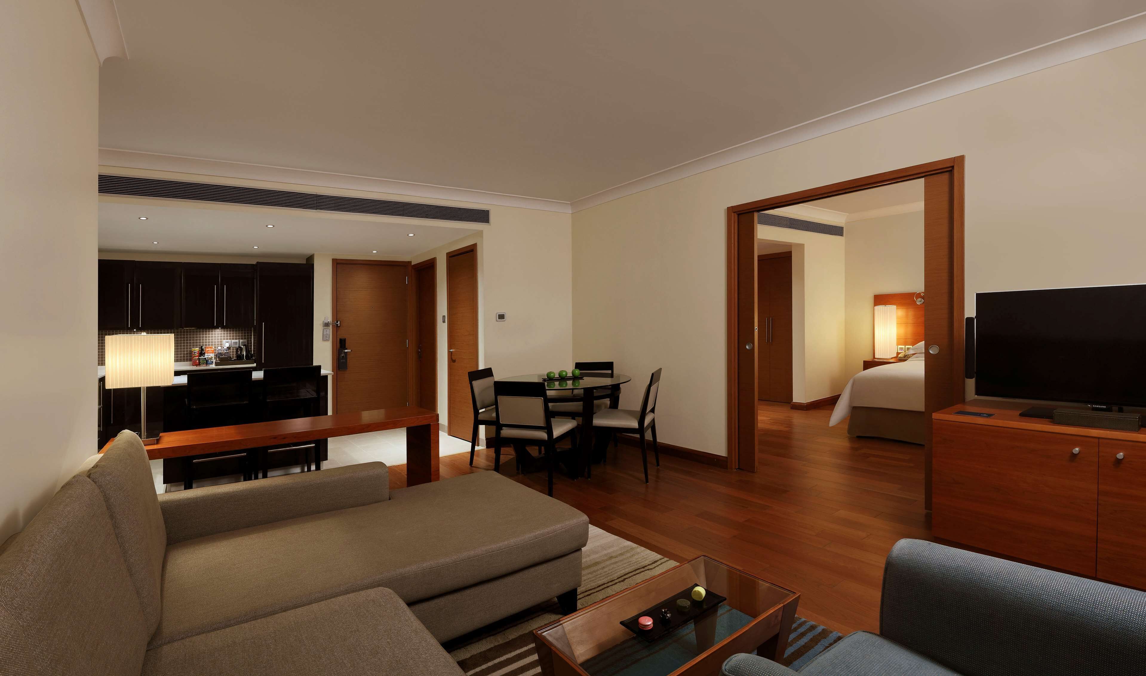 A modern hotel room with a living area, dining space, and a bedroom.