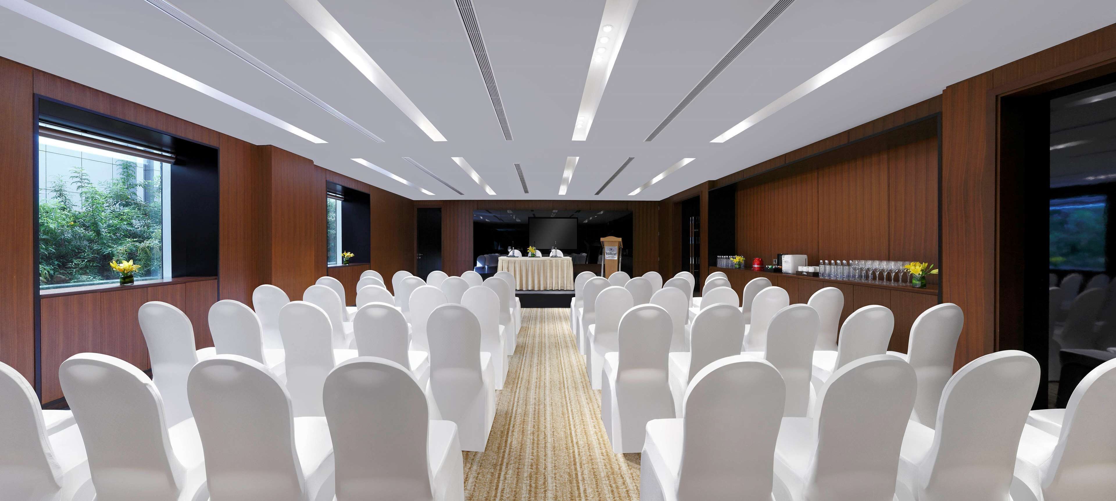 A conference room with rows of white chairs, a stage with a podium, and a buffet table with food and drinks.