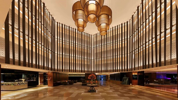 A spacious lobby with a high ceiling, vertical wooden slats, a central chandelier, and a reception desk. - Hilton Bangalore Embassy GolfLinks (Bengaluru)
