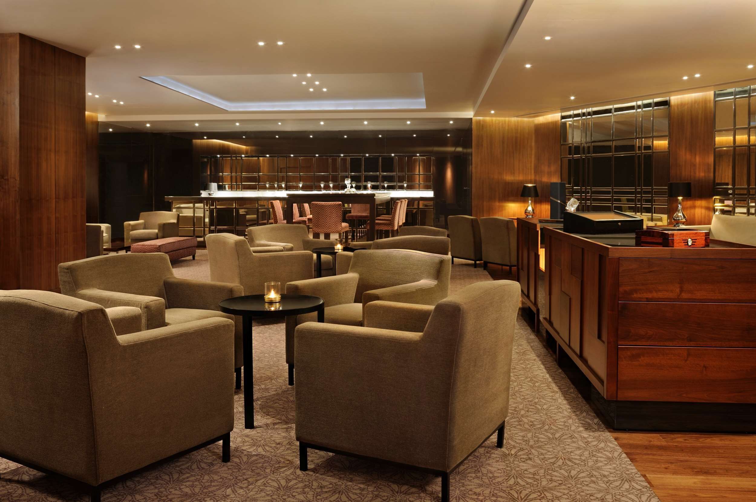 A modern lounge area with sofas, a coffee table, and a bar area with wooden cabinets and a large mirror.