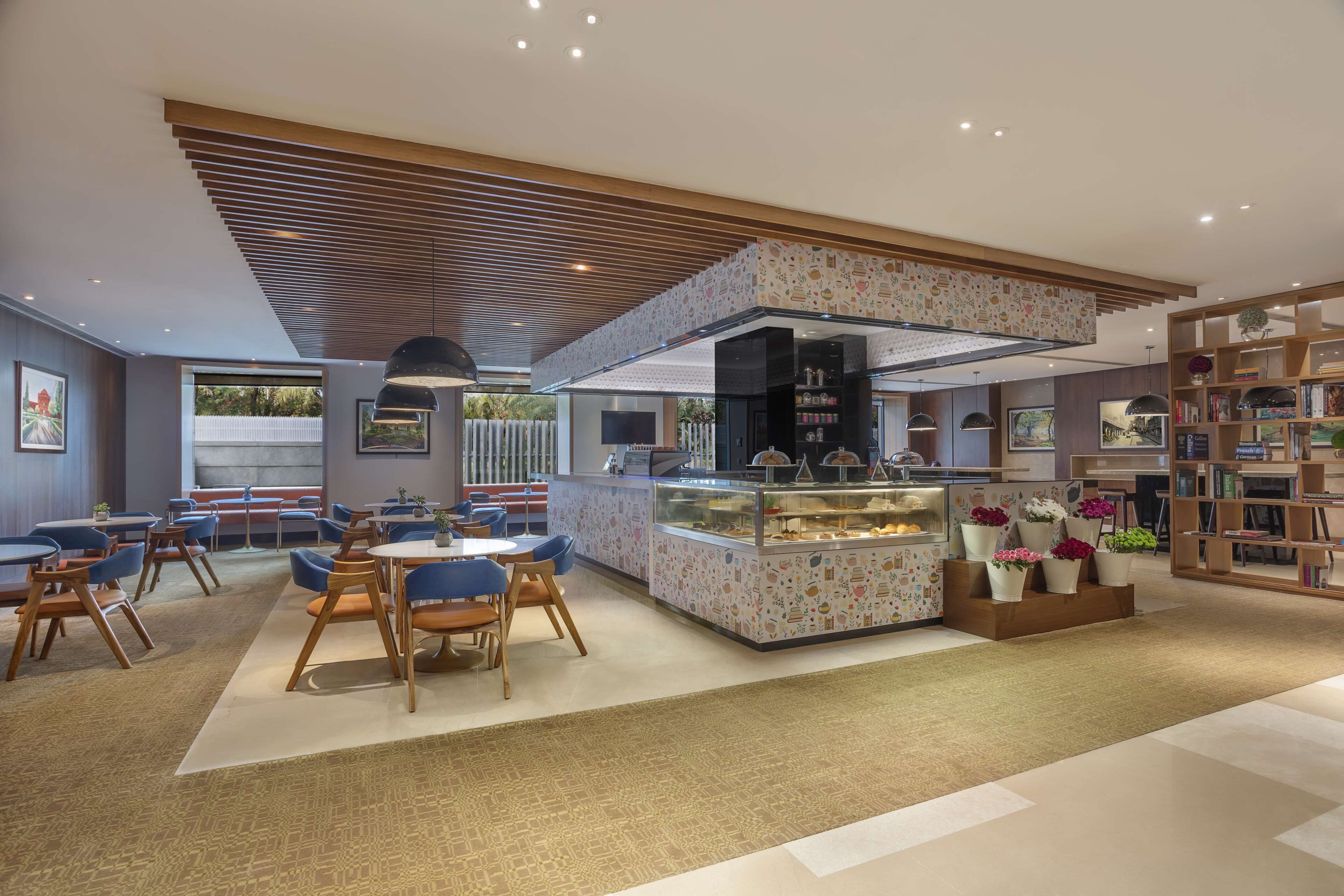 A modern restaurant with a central counter, seating area, and a bookshelf.