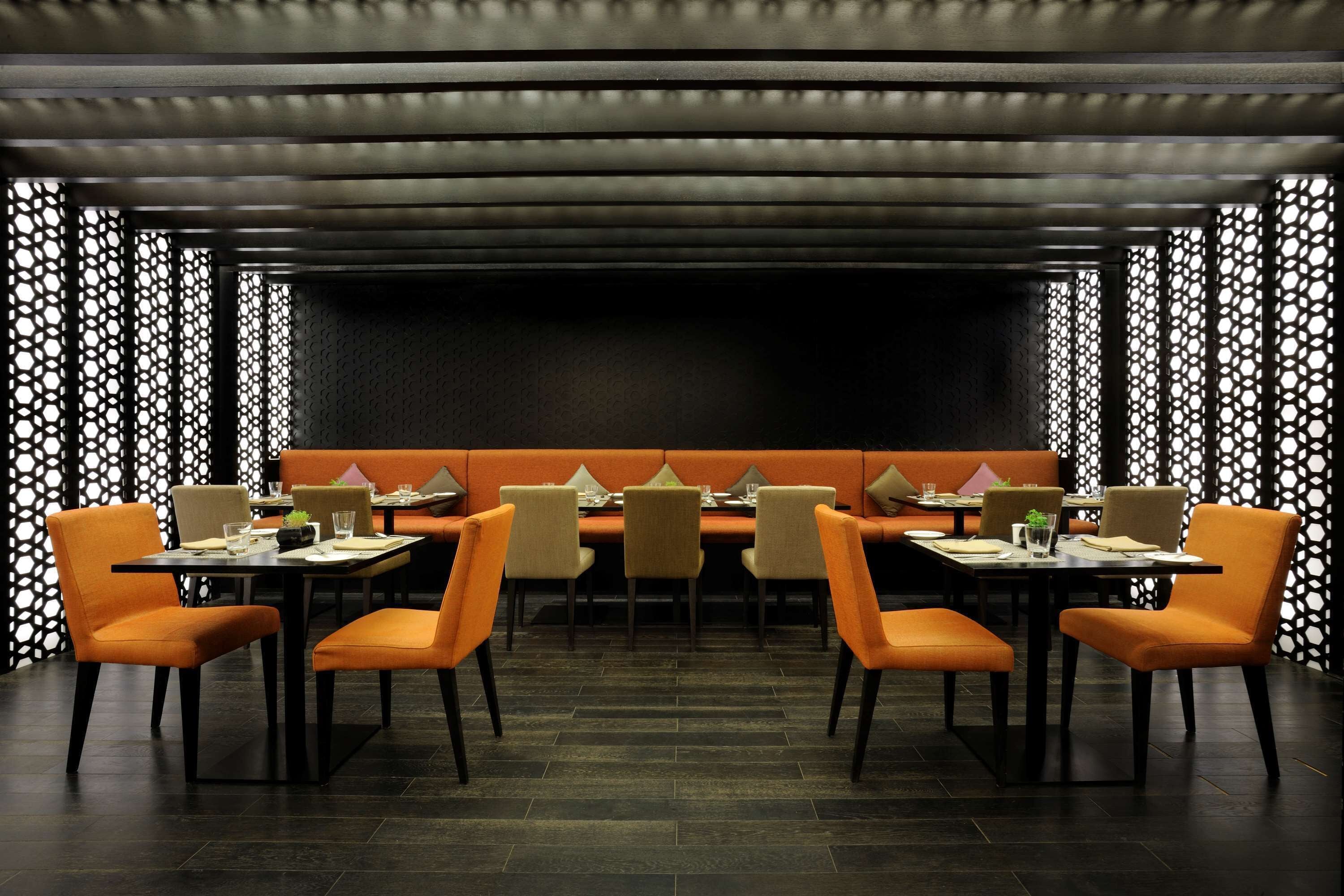 A restaurant with a long table and orange chairs, surrounded by a patterned wall.