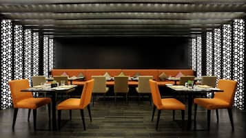 A restaurant with a long table and orange chairs, surrounded by a patterned wall.
