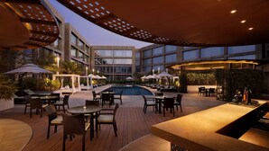 A modern outdoor pool area with lounge chairs and umbrellas, surrounded by a building with large windows. - Hilton Bangalore Embassy GolfLinks (Bengaluru)