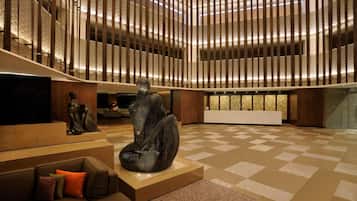 Un vestíbulo amplio con un diseño moderno, que presenta una escultura central, una zona de estar con sofá y cojines, y un patrón de suelo a cuadros.