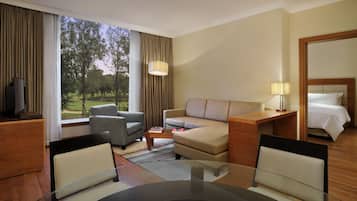 A hotel room with a sofa, armchairs, a dining table, a TV, a lamp, and a bed.