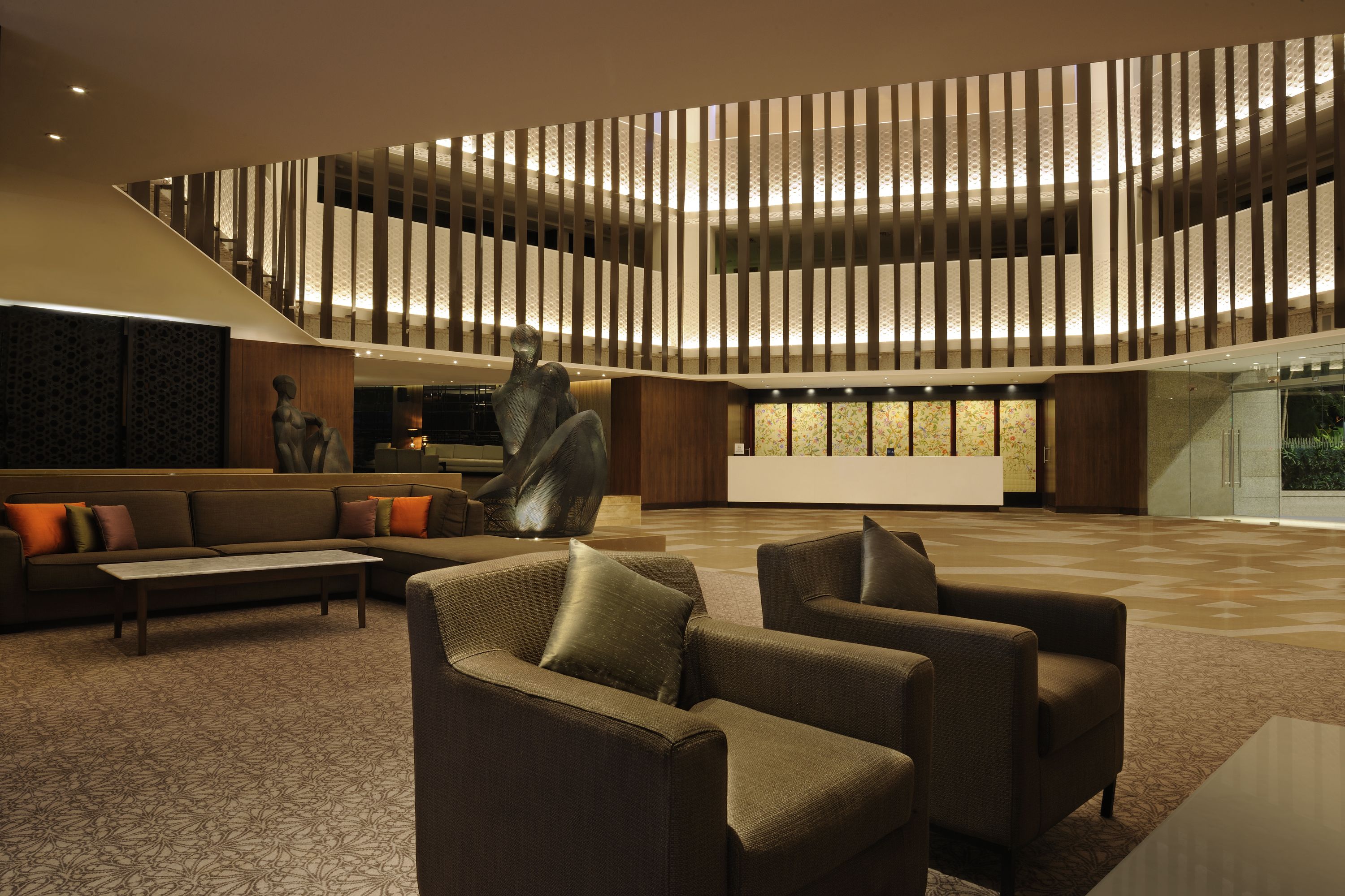 A spacious lobby with a modern design, featuring a large seating area with sofas and armchairs, a decorative sculpture, and a patterned carpet.