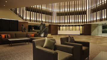 A spacious lobby with a modern design, featuring a large seating area with sofas and armchairs, a decorative sculpture, and a patterned carpet.