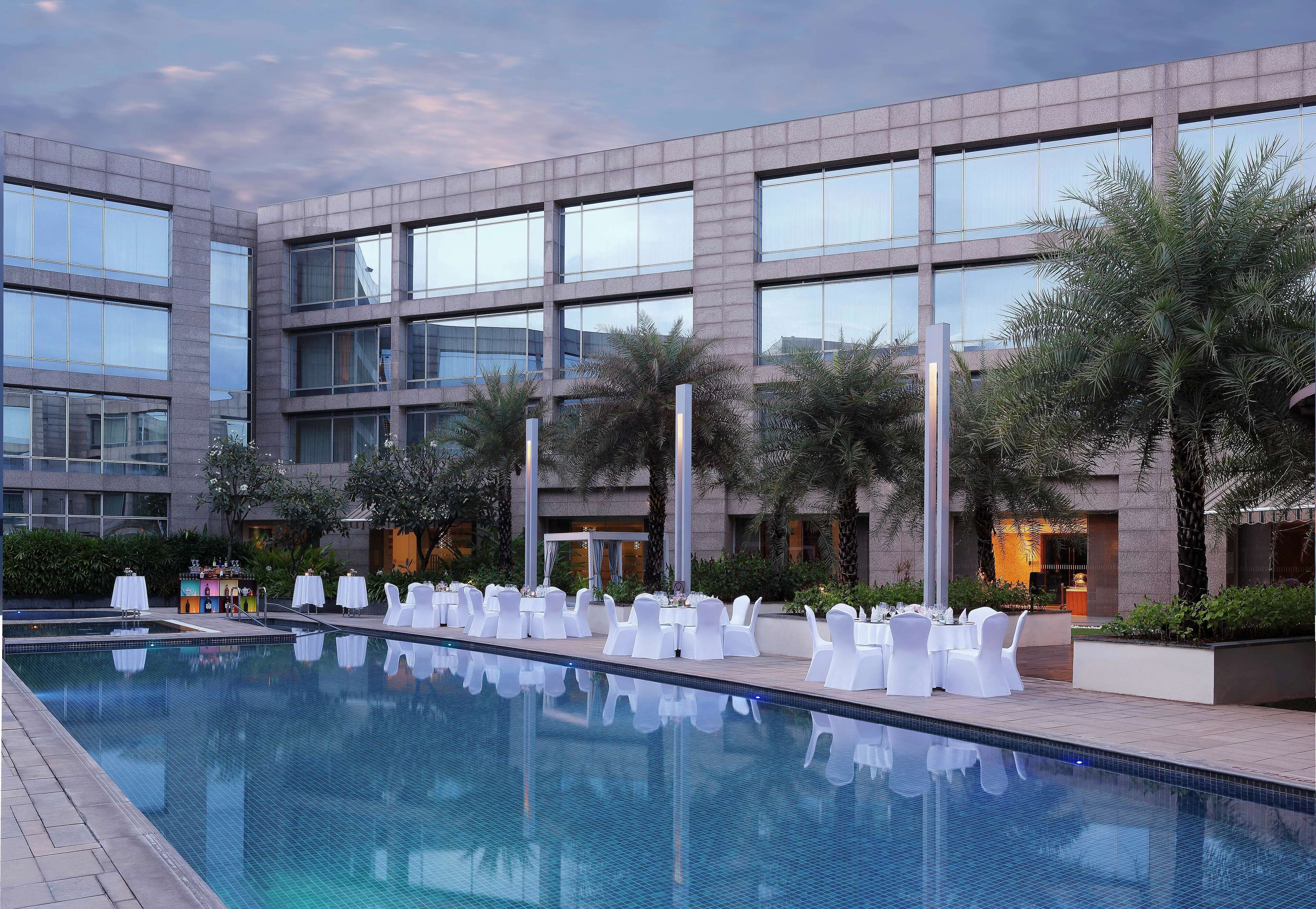 A modern hotel with a large pool, white lounge chairs, and palm trees.