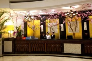 Zona de recepción de un hotel, con mostrador, dos empleados y ramas decorativas de cerezo.