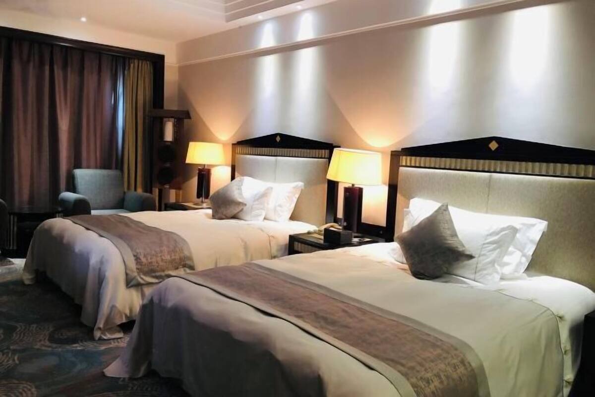 Habitación de hotel con dos camas, una silla y un escritorio con lámparas.