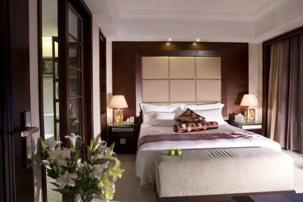 Habitación de hotel con una cama grande, dos mesitas de noche, una lámpara de noche, una ventana con cortinas y un jarrón con flores.
