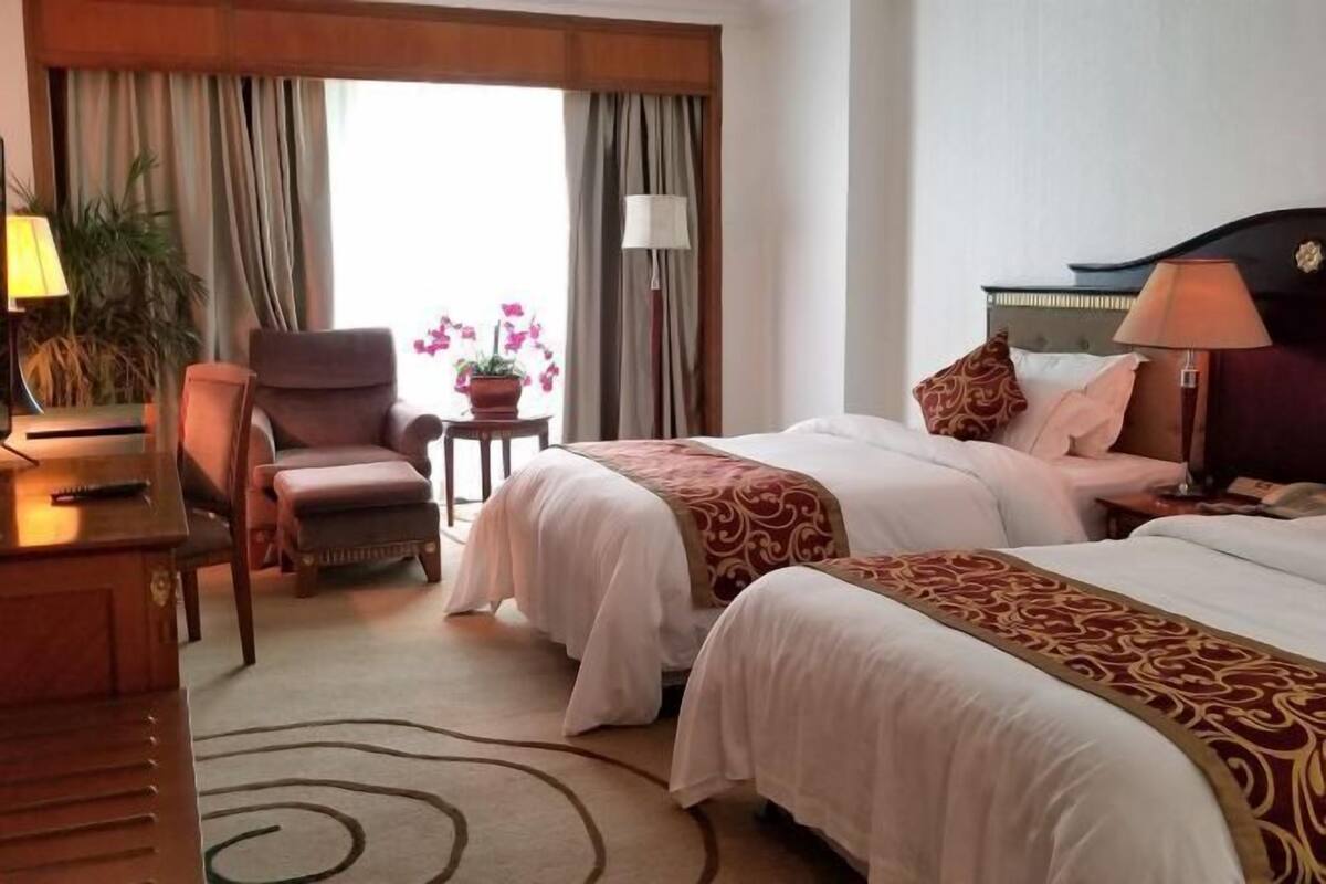 Habitación de hotel con dos camas, un escritorio, una silla, una lámpara y una ventana con cortinas.