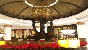 A lobby with a central sculpture, potted plants, and a reception desk.