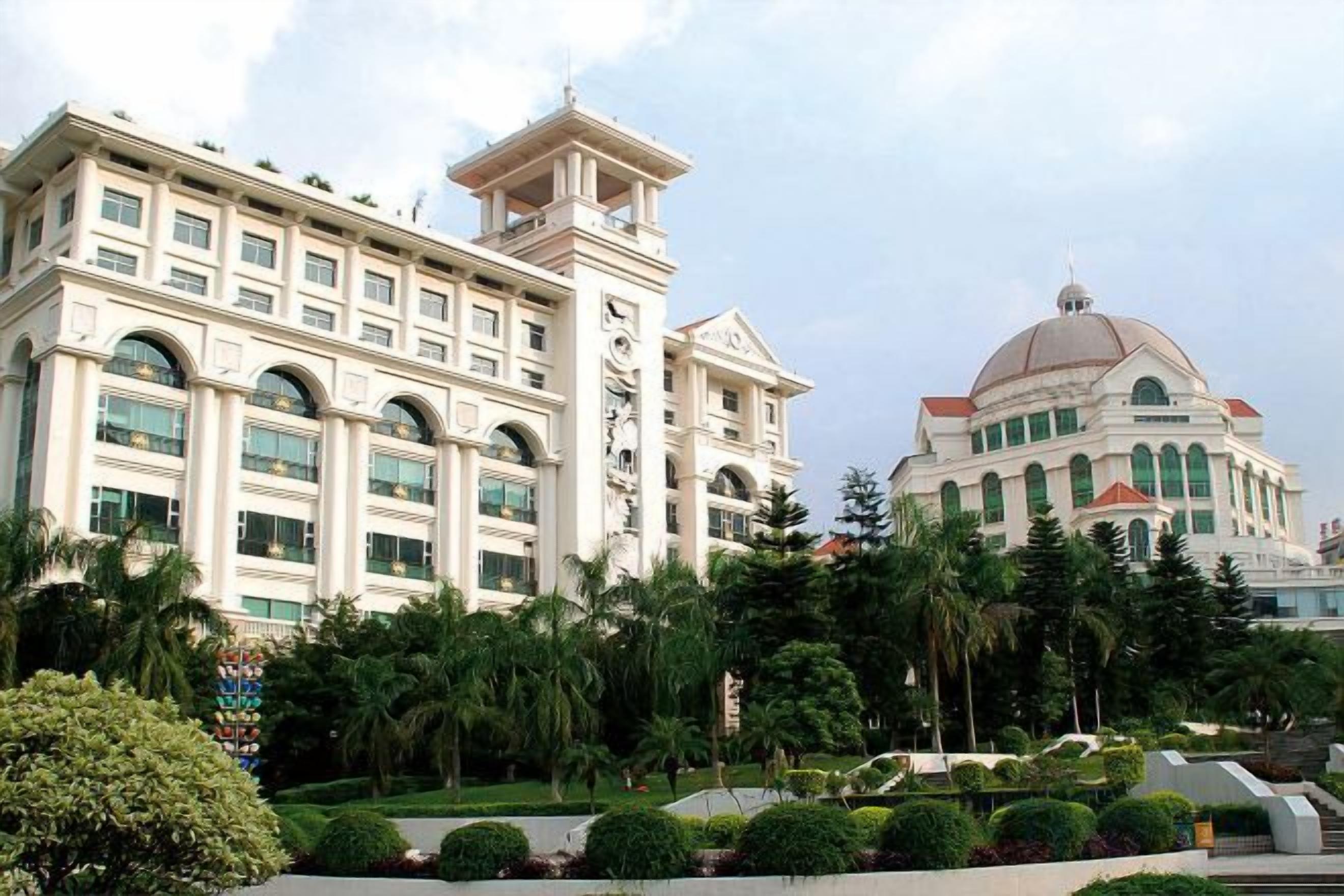 A large hotel with multiple floors, a prominent dome, and a well-maintained garden with various plants.