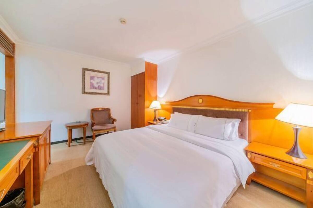 Una habitación de hotel con cama, mesita de noche, lámpara, silla y un cuadro en la pared.