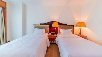 A hotel room with two single beds, a wooden headboard, bedside tables with lamps, and a nightstand.
