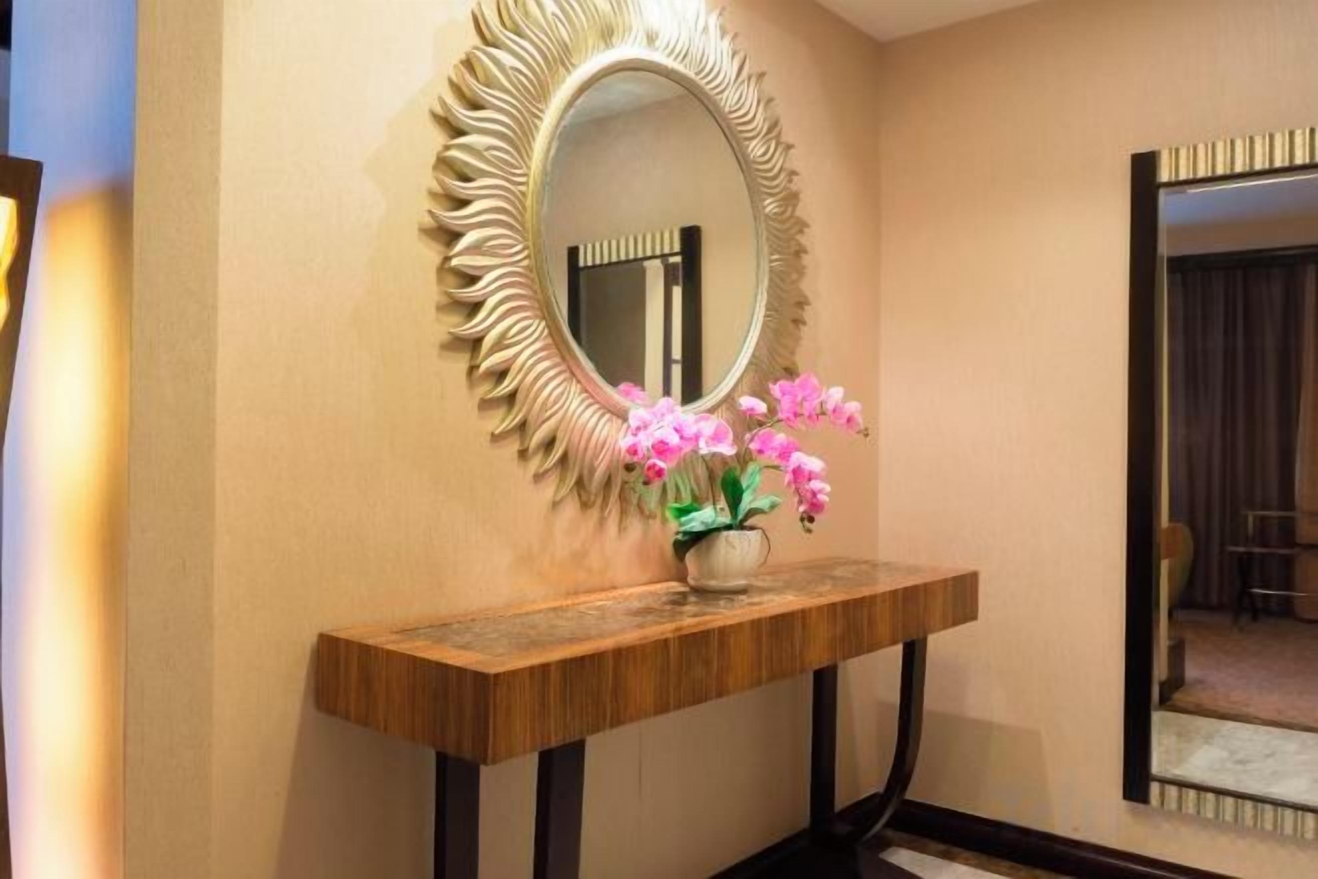 A hallway with a mirror, a wooden console table, and a vase of pink flowers.