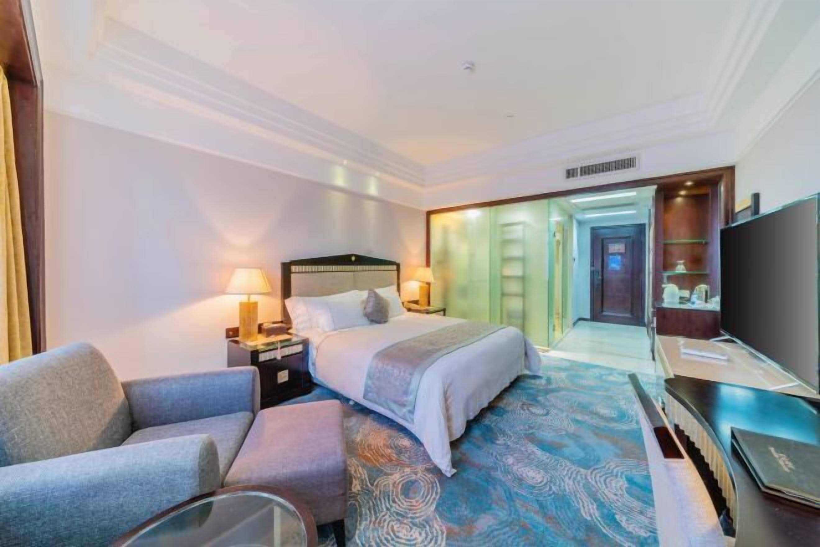 Habitación de hotel con una cama, escritorio, silla, televisor y baño visible a través de una puerta abierta.