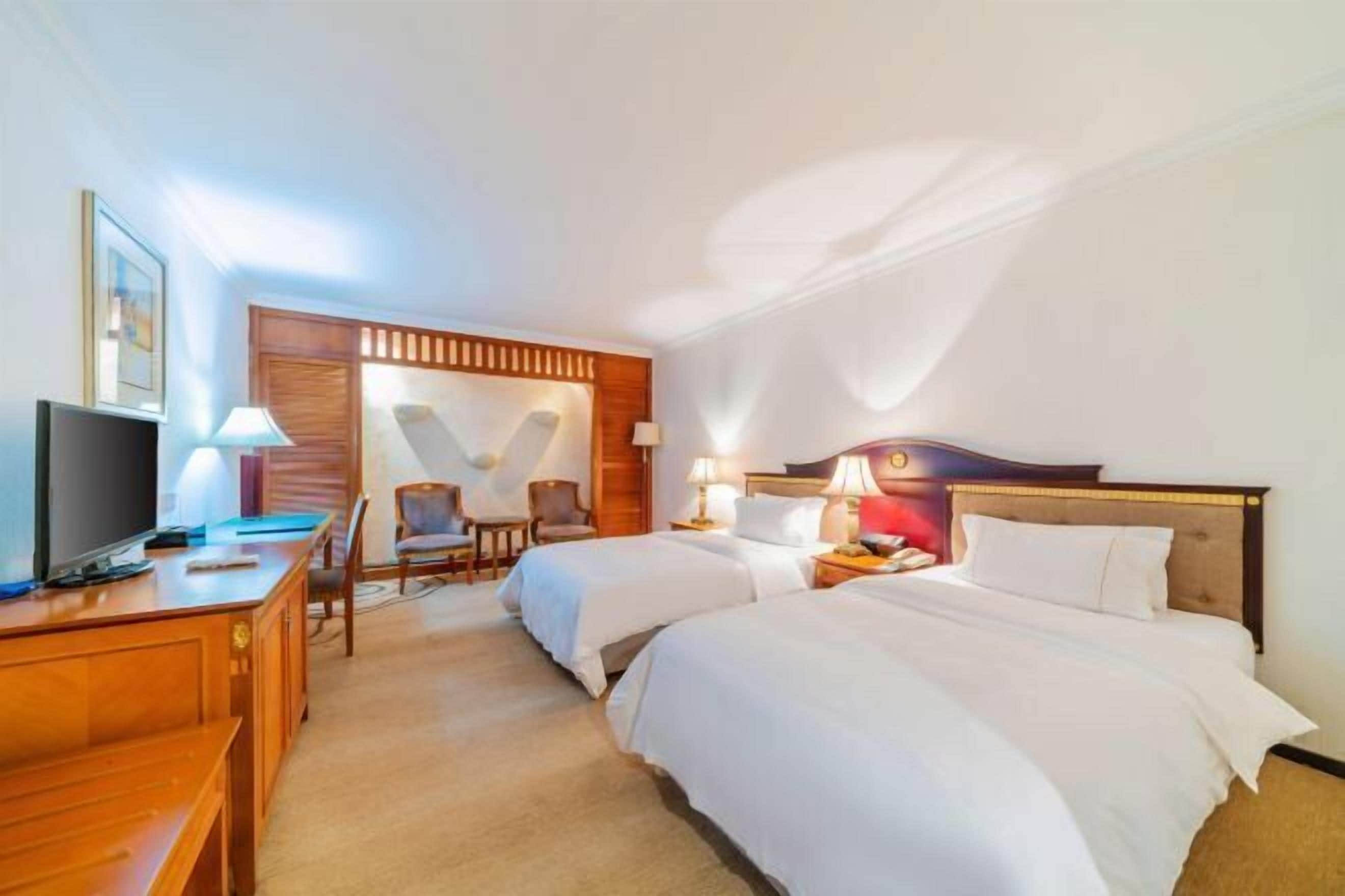 A hotel room with two beds, a desk with a television, and a chair.