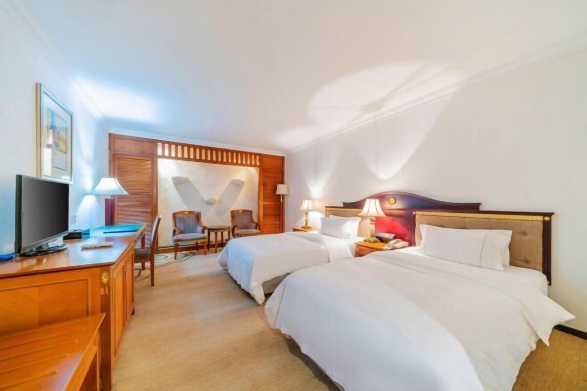 A hotel room with two beds, a desk with a television, and a chair.