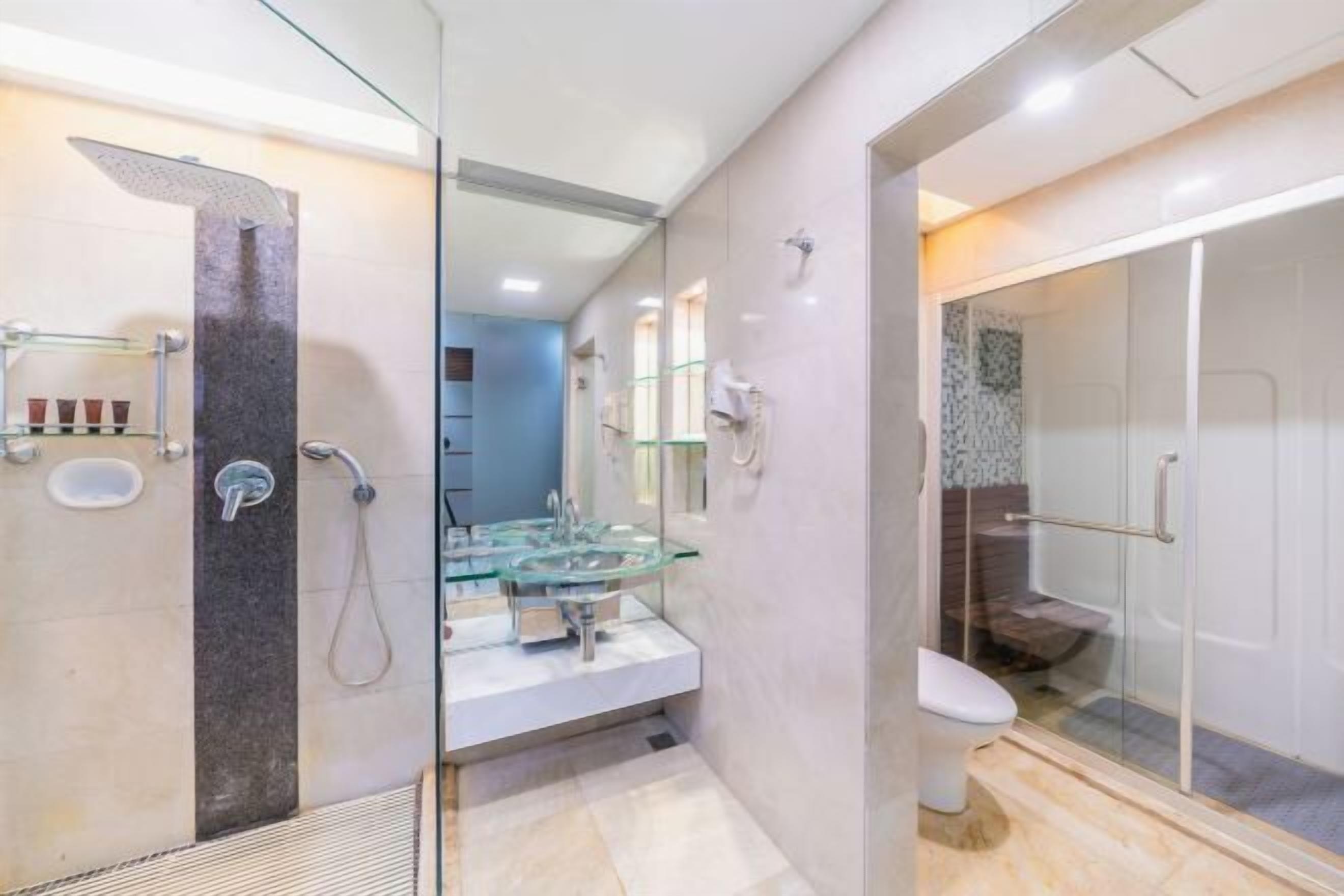 Un baño moderno con cabina de ducha de vidrio, lavamanos de vidrio y un inodoro blanco.