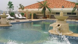 A swimming pool with water fountains, lounge chairs, and palm trees.