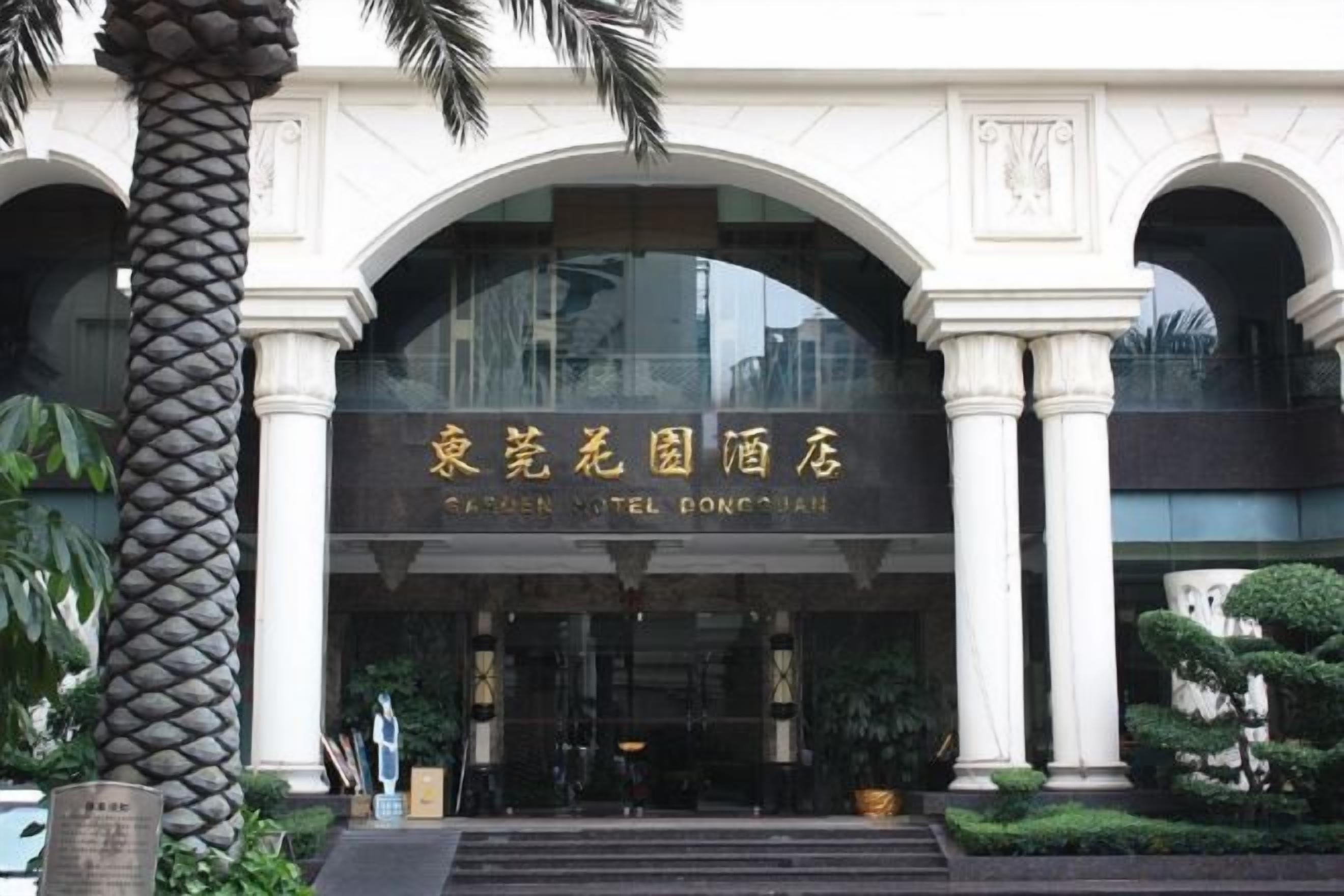 A hotel entrance with an arched facade, palm trees, and a sign in a foreign language.