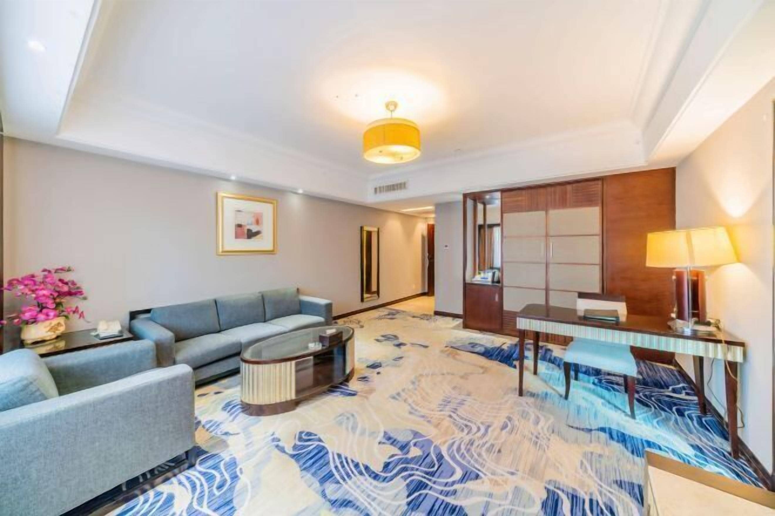 Habitación de hotel con sofá, una mesita de centro, escritorio con lámpara y alfombra estampada.