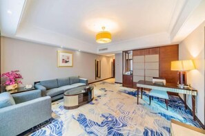 A hotel room with a sofa, a coffee table, a desk with a lamp, and a patterned carpet.