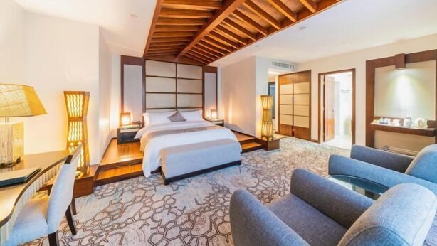 A hotel room with a bed, two bedside tables, a desk, a chair, a sofa, and a large mirror.