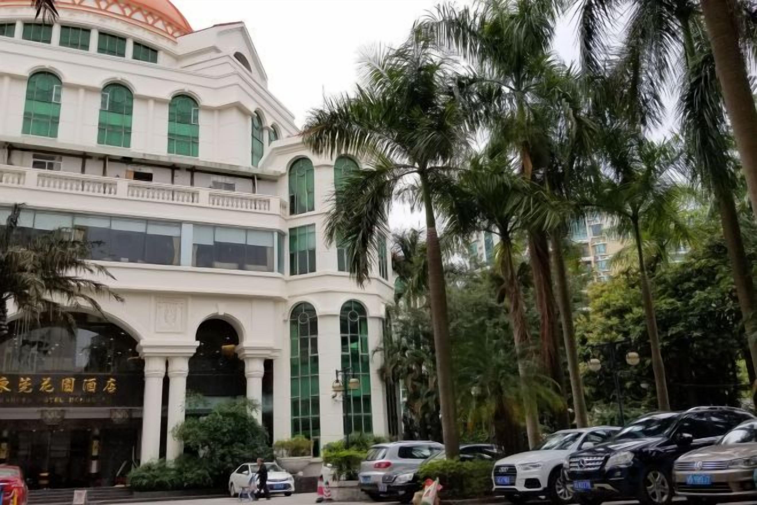A multi-story building with a white facade and green windows, surrounded by palm trees.