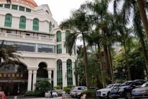 A multi-story building with a white facade and green windows, surrounded by palm trees. - Garden Hotel Dongguan (Dongguan)